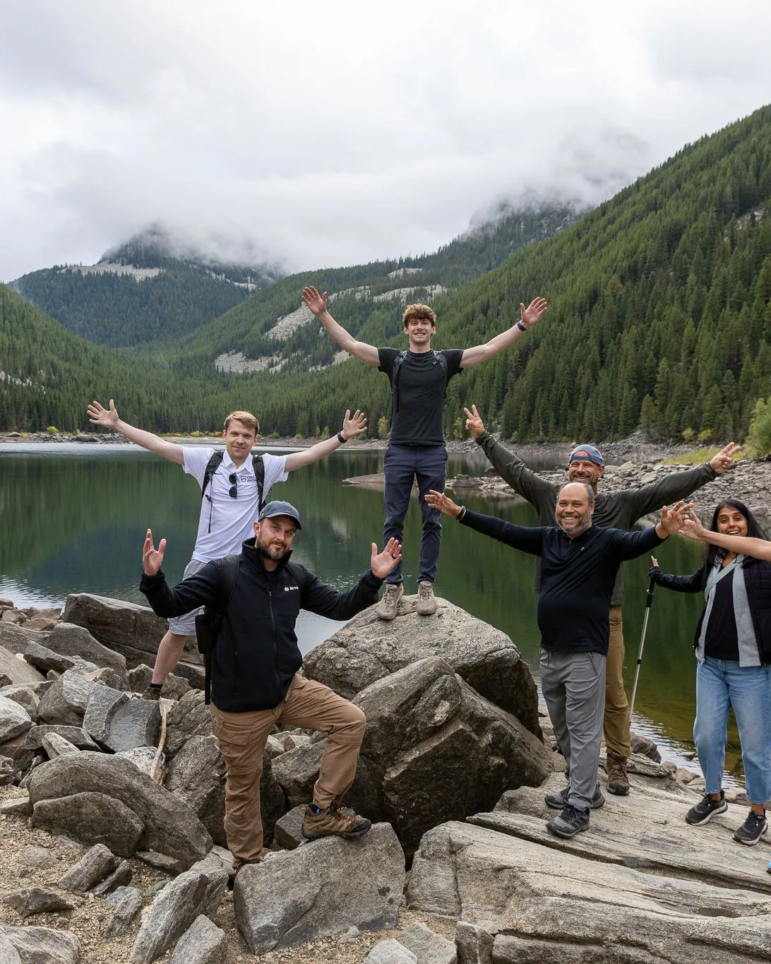 CIO Ascent members celebrating on a rocky lakeshore below forested mountains