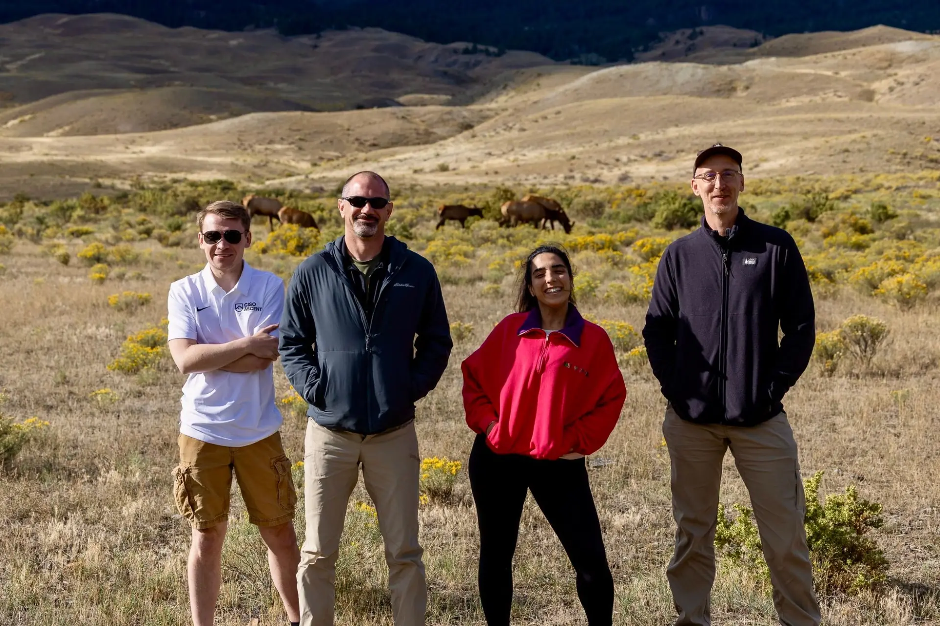 Retreat attendees smiling in a sagebrush meadow with elk grazing behind them